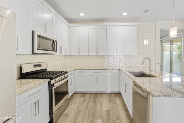 kitchen with stainless steel appliances, a sink, a peninsula, white cabinets, and light wood-style flooring