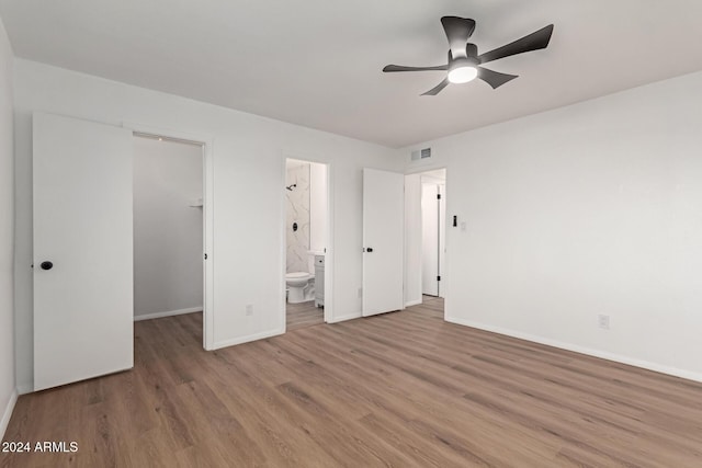 unfurnished bedroom with ensuite bath, ceiling fan, light hardwood / wood-style flooring, a spacious closet, and a closet