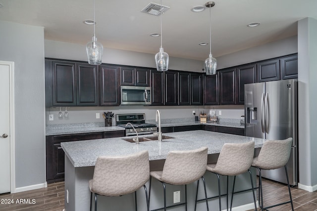 kitchen featuring dark hardwood / wood-style flooring, appliances with stainless steel finishes, a breakfast bar area, and an island with sink