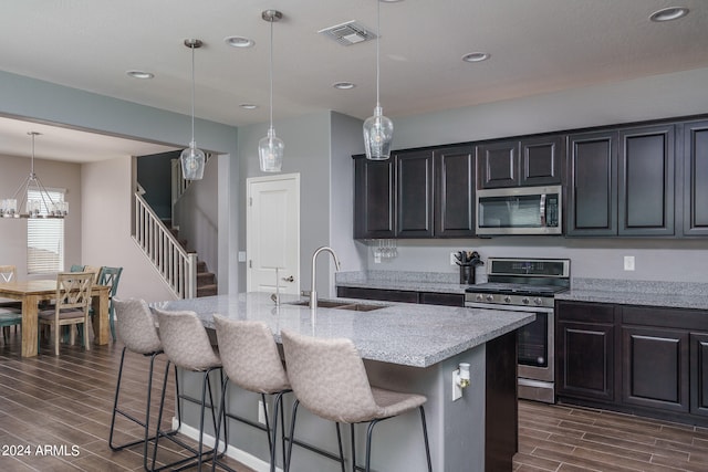 kitchen featuring decorative light fixtures, appliances with stainless steel finishes, sink, dark wood-type flooring, and a kitchen island with sink