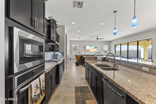 kitchen with light stone countertops, stainless steel appliances, ceiling fan, sink, and decorative light fixtures