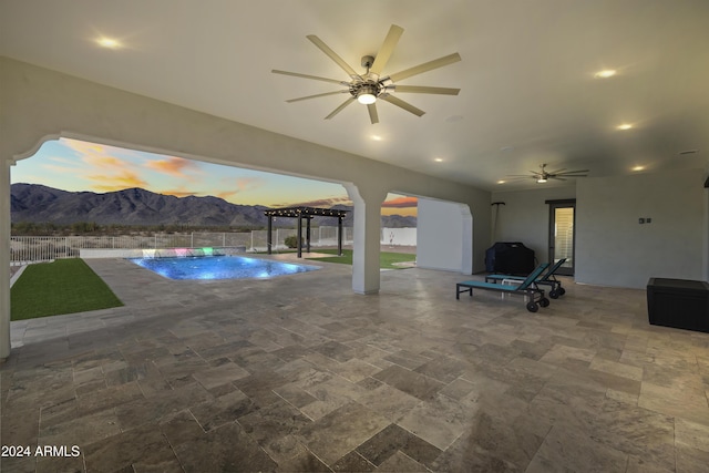 pool at dusk featuring a mountain view and ceiling fan