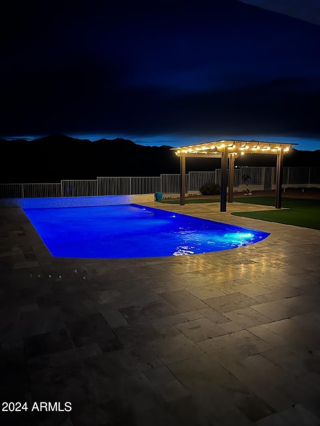 pool at night featuring a patio area