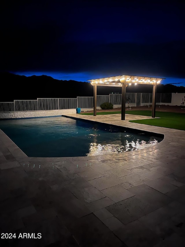 pool at night with a mountain view, a pergola, and a patio area