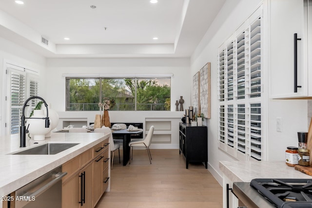kitchen featuring a sink, stainless steel dishwasher, light wood finished floors, recessed lighting, and light stone countertops