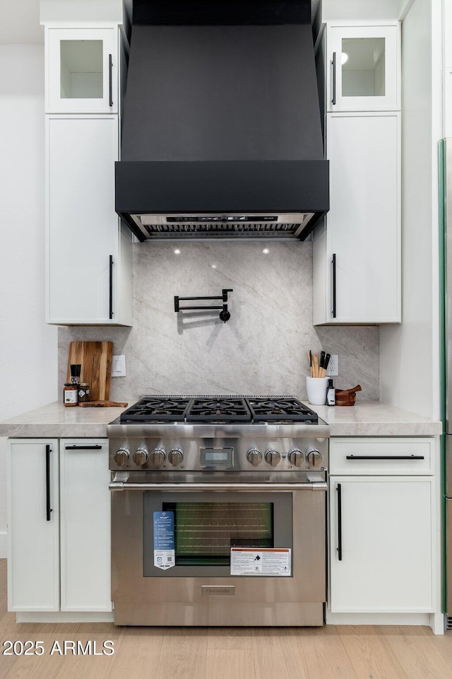 kitchen with high end stainless steel range, premium range hood, white cabinets, and light countertops