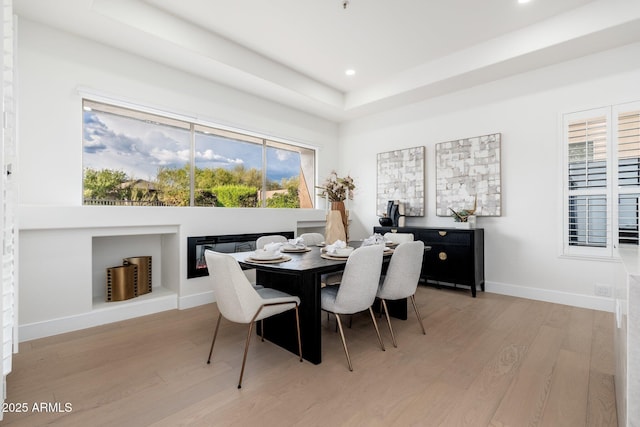 dining space featuring light wood-type flooring, baseboards, a raised ceiling, and recessed lighting
