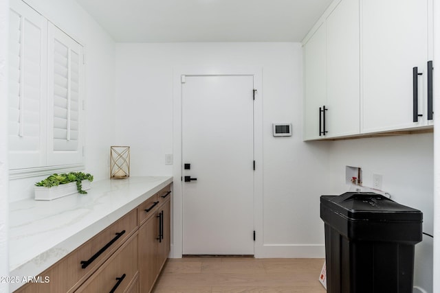 laundry area with cabinet space, washer hookup, light wood-style flooring, and baseboards