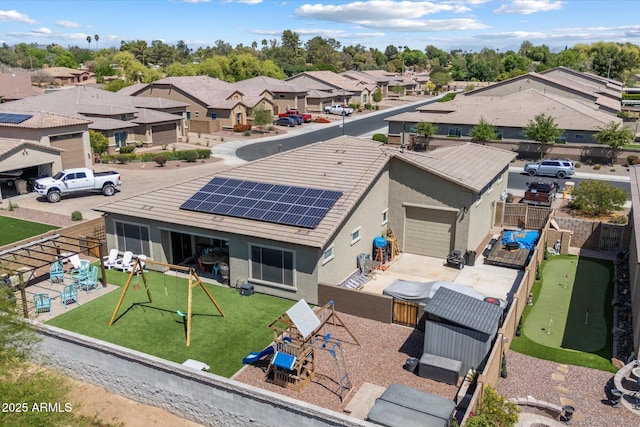 rear view of house featuring a residential view, stucco siding, a fenced backyard, and roof mounted solar panels