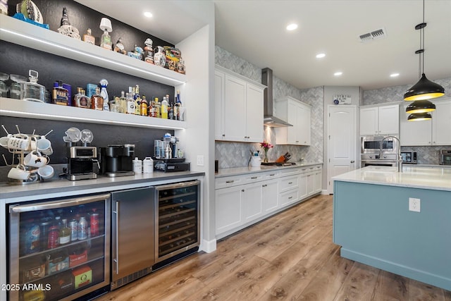 bar with wall chimney range hood, stainless steel appliances, visible vents, and wine cooler