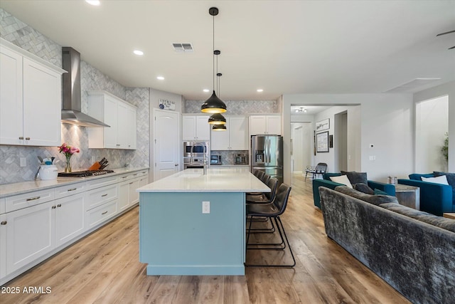 kitchen with open floor plan, white cabinetry, visible vents, wall chimney exhaust hood, and appliances with stainless steel finishes