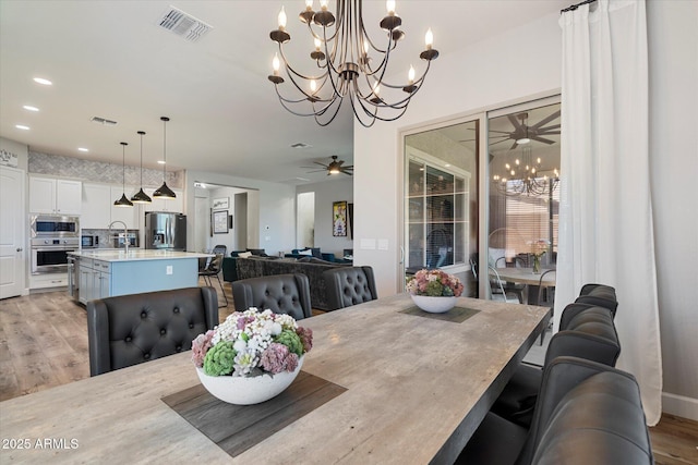 dining space with visible vents, recessed lighting, light wood-style floors, and ceiling fan with notable chandelier
