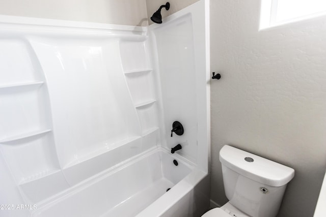 bathroom featuring toilet, shower / bath combination, and a textured wall