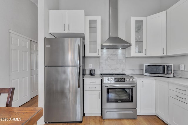 kitchen featuring appliances with stainless steel finishes, wall chimney range hood, white cabinets, and decorative backsplash