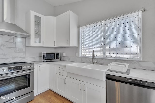 kitchen featuring sink, appliances with stainless steel finishes, white cabinetry, light hardwood / wood-style floors, and wall chimney exhaust hood