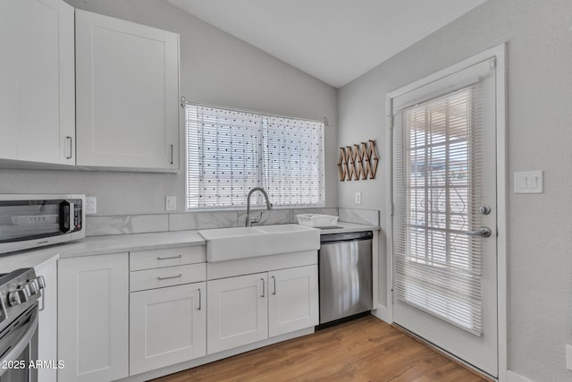 kitchen featuring stainless steel appliances, white cabinetry, lofted ceiling, and sink