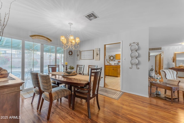 dining space featuring light wood-type flooring, baseboards, visible vents, and a chandelier