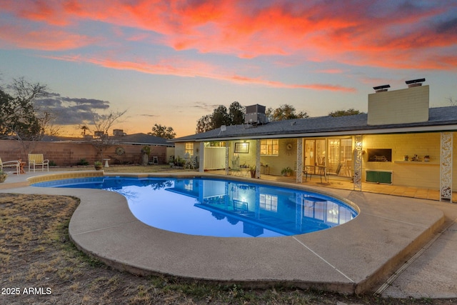 pool at dusk with an outdoor pool, a patio, and fence