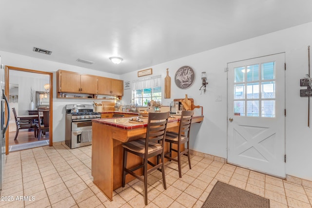 kitchen featuring visible vents, double oven range, tile countertops, and a peninsula