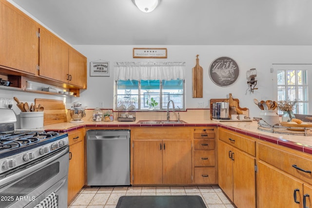 kitchen with light tile patterned floors, appliances with stainless steel finishes, a sink, and tile counters