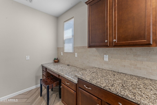 kitchen featuring light parquet flooring, light stone countertops, backsplash, and built in desk