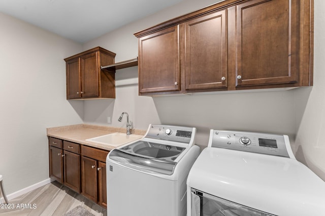 laundry room with cabinets, sink, light wood-type flooring, and washing machine and dryer