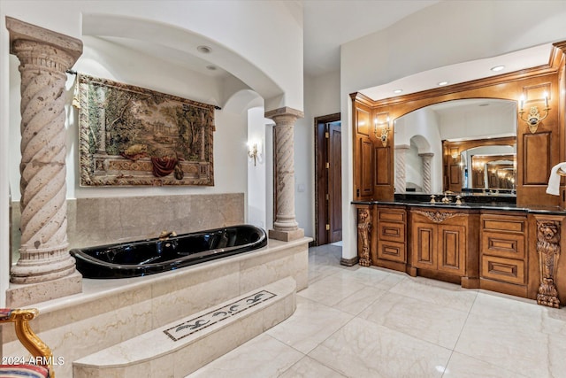 bathroom featuring tile floors, oversized vanity, ornate columns, and tiled tub