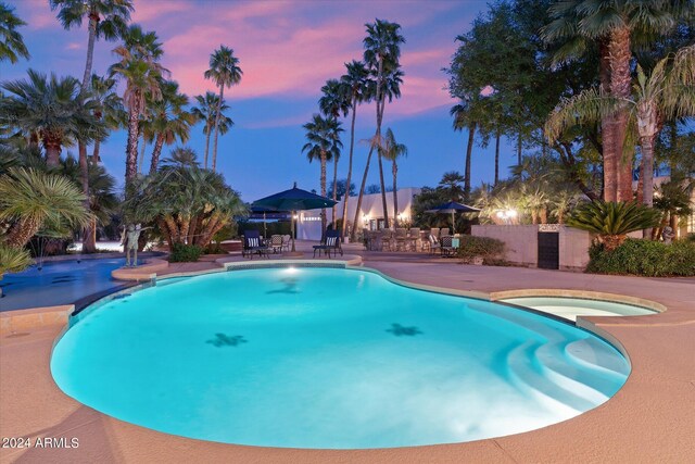 pool at dusk featuring a patio area and an in ground hot tub