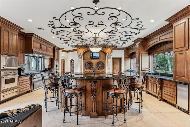 kitchen featuring light tile floors, a kitchen island with sink, ornamental molding, hanging light fixtures, and oven