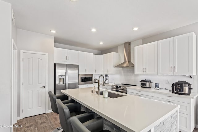 kitchen with wall chimney range hood, a sink, stainless steel appliances, light wood finished floors, and white cabinetry