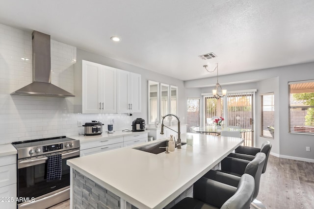 kitchen featuring wall chimney exhaust hood, light wood finished floors, a sink, stainless steel electric range, and visible vents