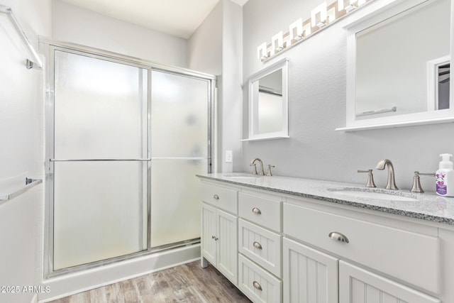 bathroom featuring a shower stall, wood finished floors, a sink, and double vanity