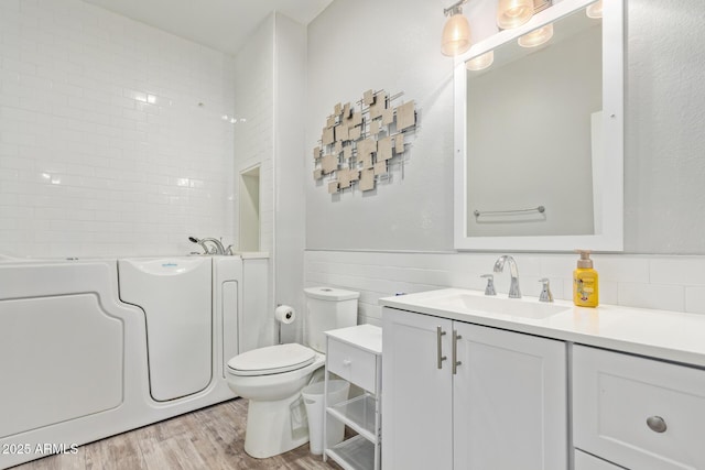 bathroom with a washtub, wood finished floors, vanity, washer / dryer, and toilet