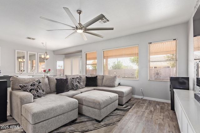 living area featuring ceiling fan with notable chandelier, light wood-style flooring, visible vents, and a healthy amount of sunlight
