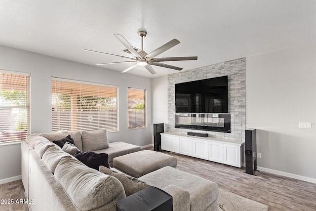 living area featuring plenty of natural light, a ceiling fan, baseboards, and light wood-style floors