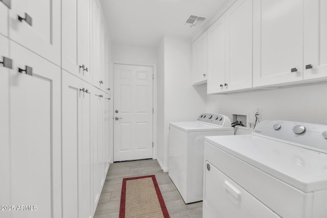 washroom featuring visible vents, cabinet space, light wood finished floors, and separate washer and dryer