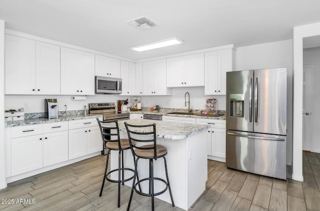 kitchen with light stone counters, stainless steel appliances, a kitchen island, a sink, and white cabinetry