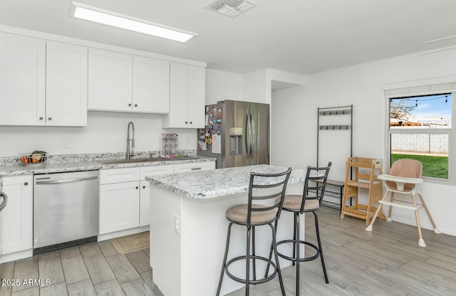 kitchen with stainless steel appliances, a kitchen island, visible vents, a sink, and white cabinetry