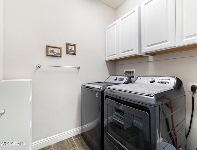 washroom with dark wood-type flooring, washing machine and dryer, and cabinets