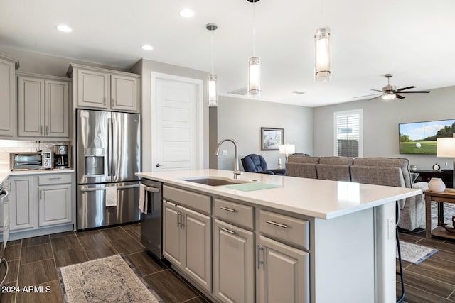 kitchen with gray cabinets, a breakfast bar, a center island with sink, sink, and appliances with stainless steel finishes