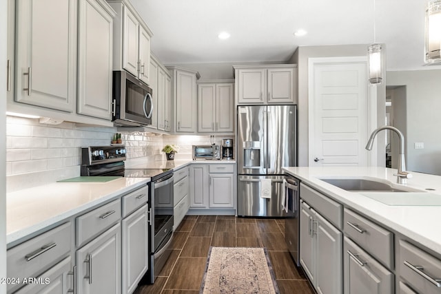 kitchen with gray cabinets, decorative light fixtures, sink, stainless steel appliances, and backsplash