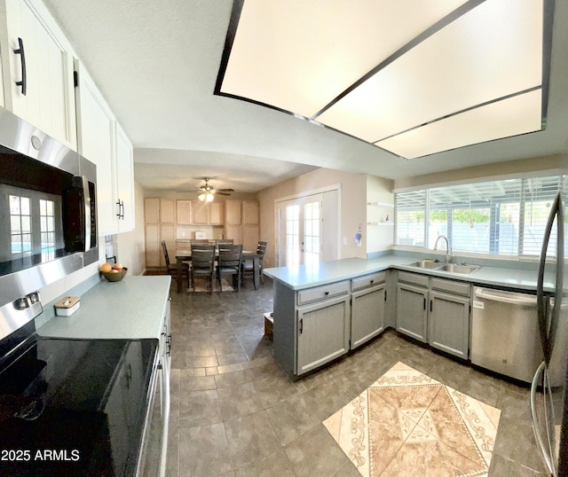kitchen featuring a peninsula, gray cabinets, appliances with stainless steel finishes, a sink, and light countertops