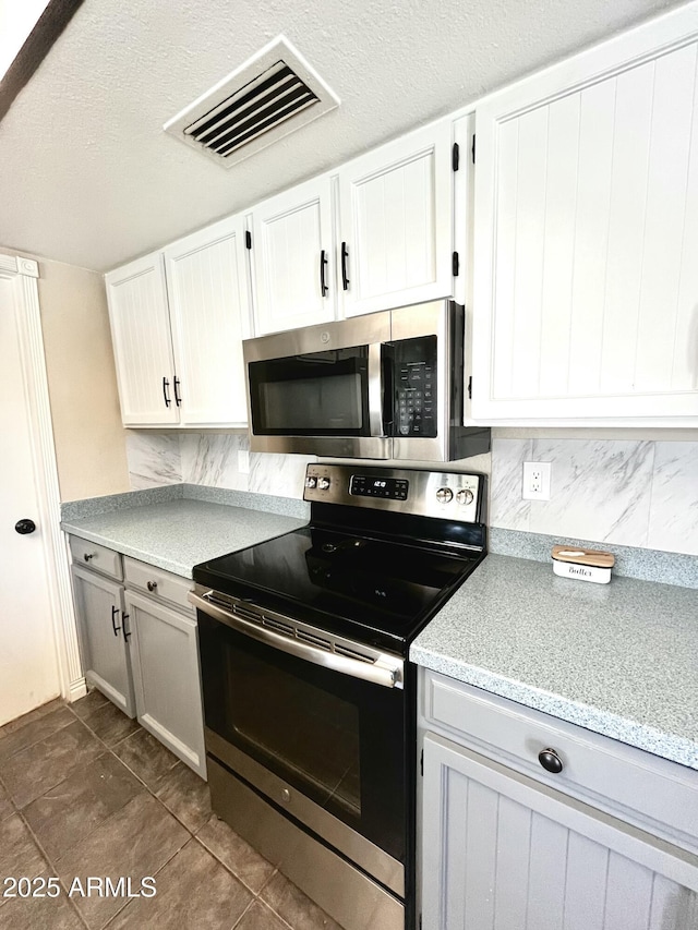 kitchen with white cabinetry, visible vents, light stone counters, stainless steel appliances, and backsplash