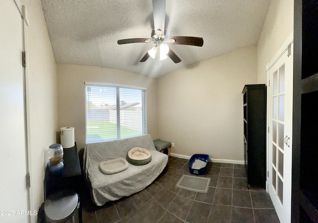 living area with baseboards, a textured ceiling, a ceiling fan, lofted ceiling, and dark tile patterned flooring