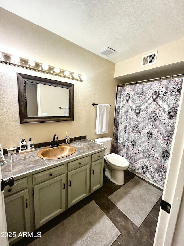 full bath with a textured ceiling, vanity, tile patterned flooring, visible vents, and toilet