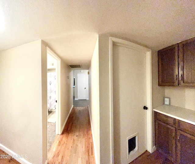 hall with visible vents, light wood-style flooring, baseboards, and a textured ceiling