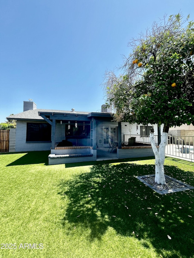 back of house featuring a yard, fence, and a chimney