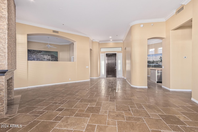 foyer with a stone fireplace, crown molding, ceiling fan, and a wealth of natural light