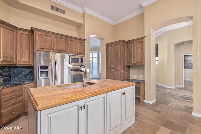 kitchen with wooden counters, appliances with stainless steel finishes, a kitchen island with sink, crown molding, and sink