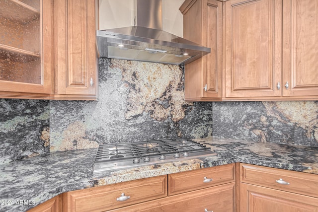 kitchen featuring dark stone countertops, decorative backsplash, wall chimney exhaust hood, and stainless steel gas cooktop